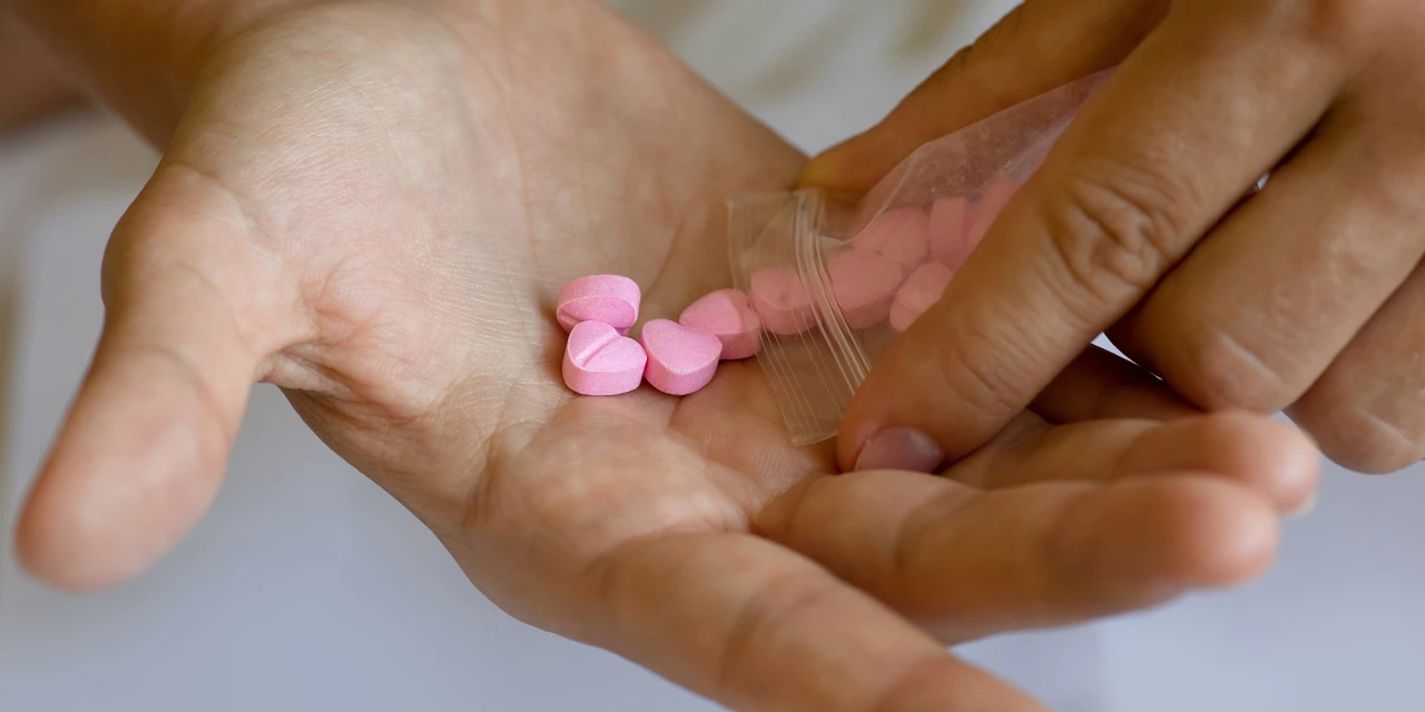 Roze pillen in hand uit zakje. Wat is XTC en waarom gebruiken mensen het?