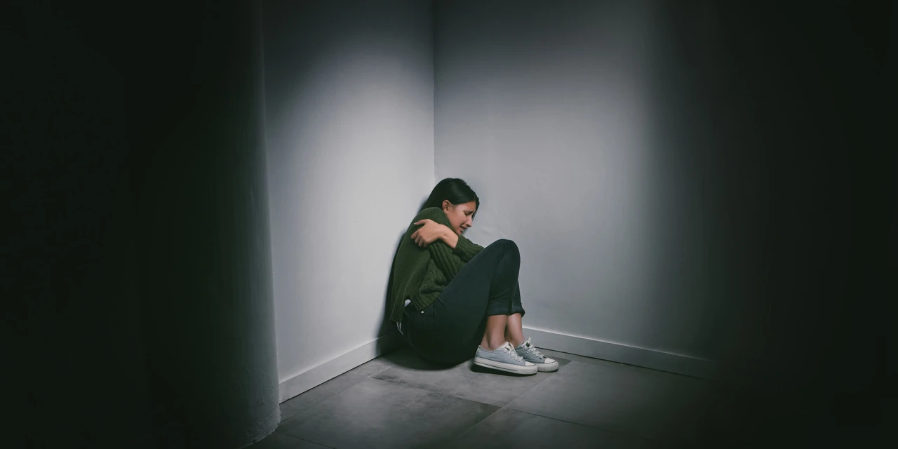 Persoon zit angstig in hoek, zichzelf omarmend, gevoel van angst en eenzaamheid.