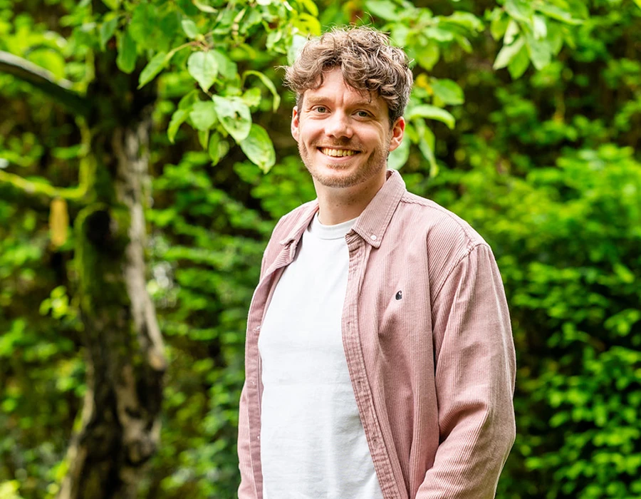 Jacob, lid van het team van Connection SGGZ, staat vriendelijk lachend in een groene omgeving.