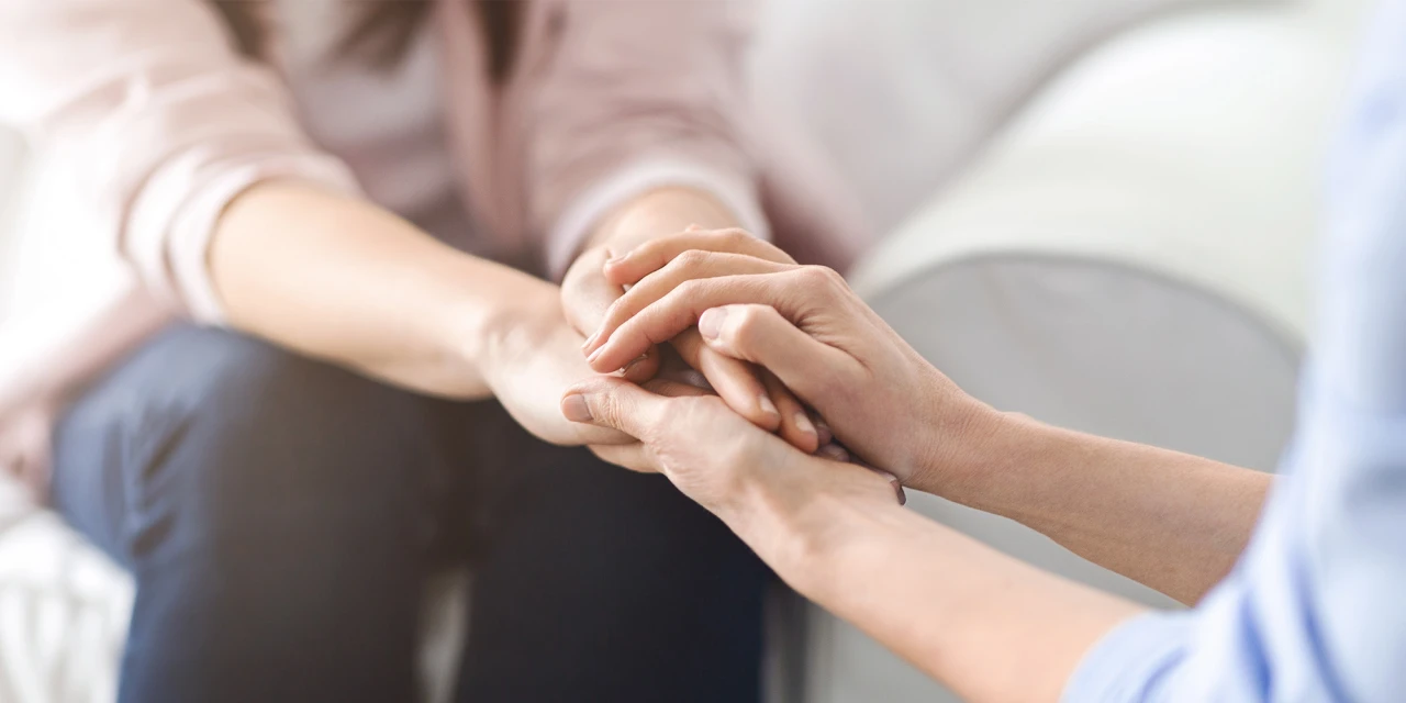Persoon houdt handen vast van ander tijdens steunend gesprek over mentale gezondheid.
