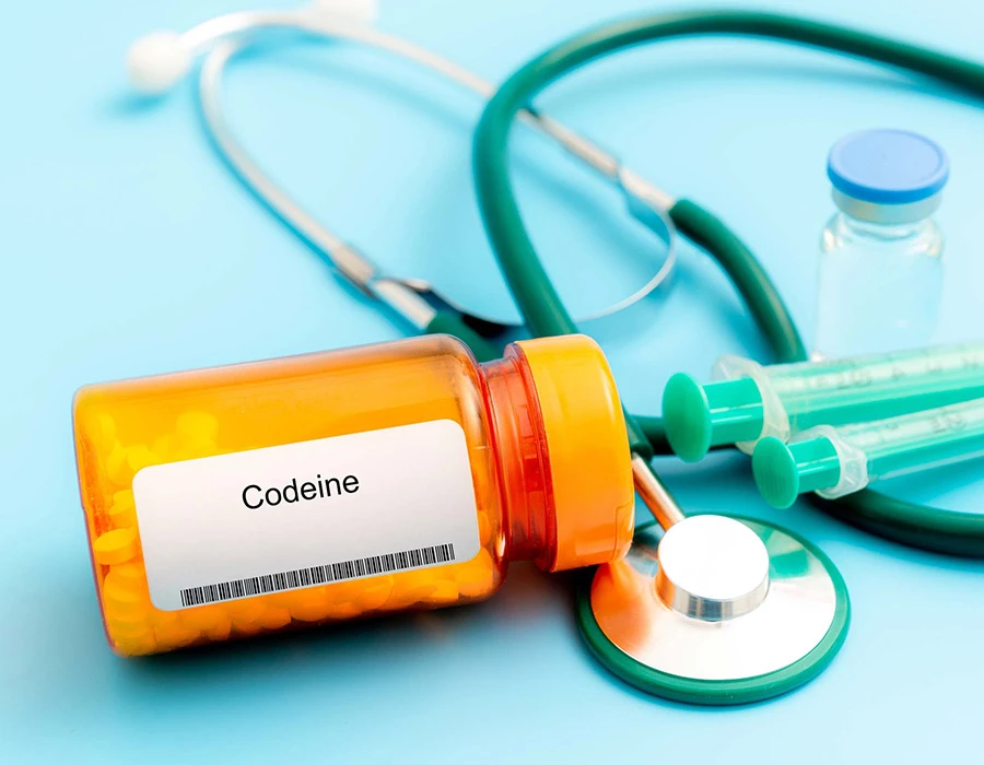 Medicijnpotje met het etiket codeïne naast een stethoscoop op een lichtblauwe ondergrond.