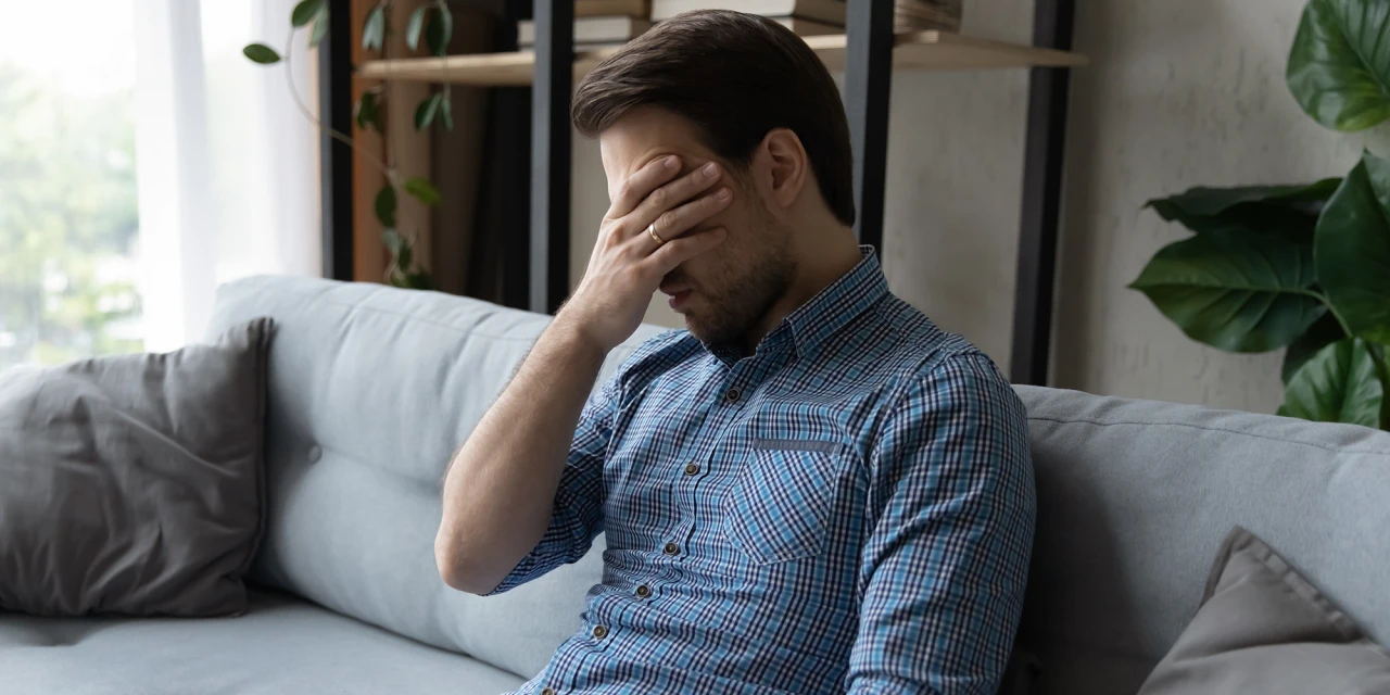 Man zit op bank met hand voor gezicht en worstelt met terugval cocaïne en schuldgevoelens.