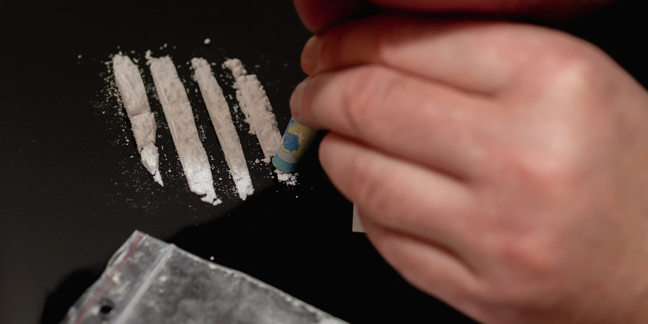 Hand met opgerold briefje bij lijnen wit poeder helpt cocaïnegebruik herkennen.