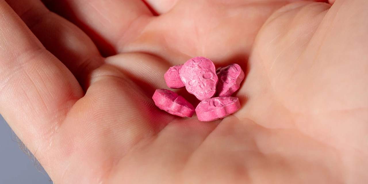 Hand met roze pillen in schedelvorm, vermoedelijk harddrugs close up.