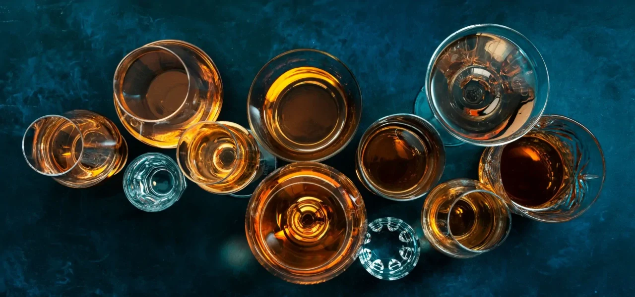 glazen-alcohol Verschillende glazen met bruine drank, van bovenaf gefotografeerd tegen een blauwe achtergrond.