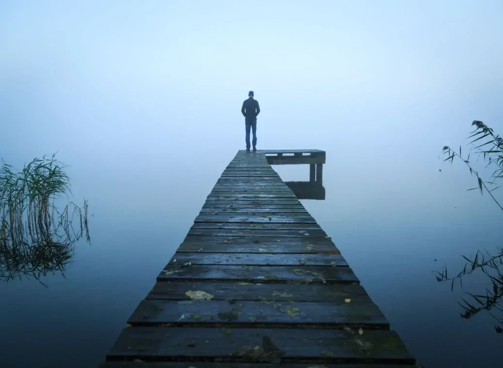Depressieve en eenzame man op een houten pier, uitkijkend over een meer met de rug naar de kijker toe.