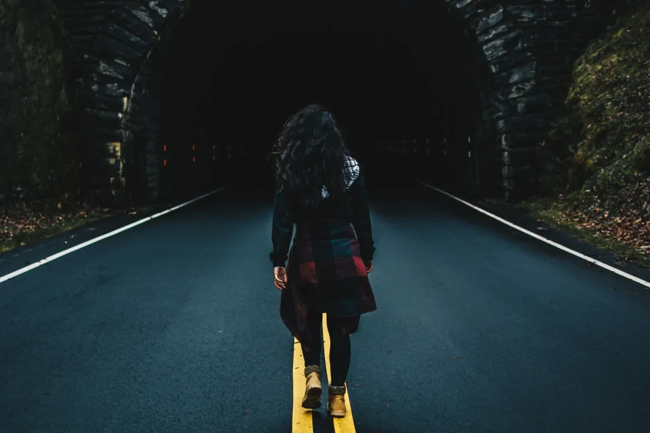 Wandelende vrouw met donker haar die richting een tunnel in de bergen loopt, over een gele streep.