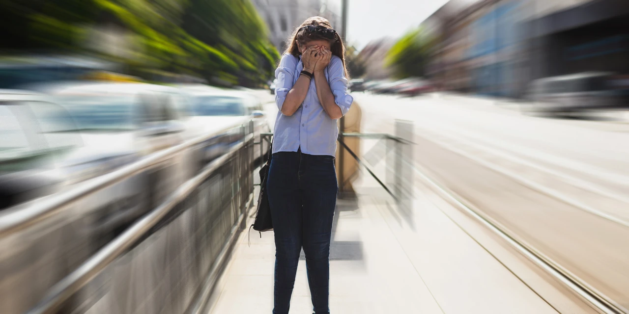 Vrouw op straat met handen voor gezicht tijdens een paniekaanval.