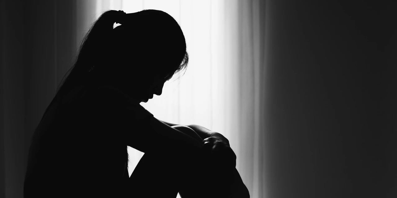 Silhouet van persoon zittend bij raam, gebogen houding, gevoel van angst en somberheid.