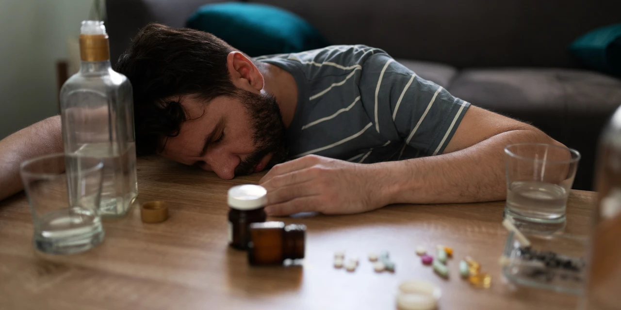Persoon ligt bewusteloos aan tafel met drugs en alcohol, out gaan door drugs.