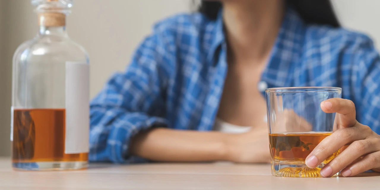 Vrouw kijkt naar glas alcohol en twijfelt over drinken of stoppen.