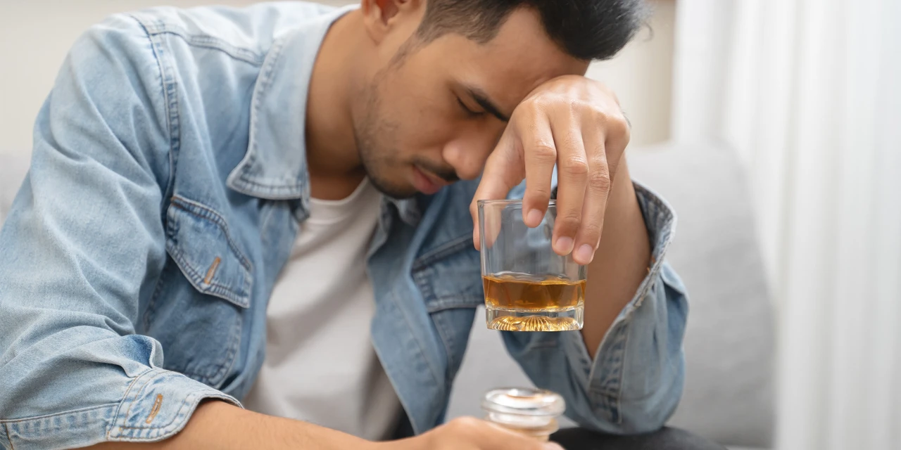 Man zit vermoeid met glas alcohol in hand, worstelend met alcoholverslaving.