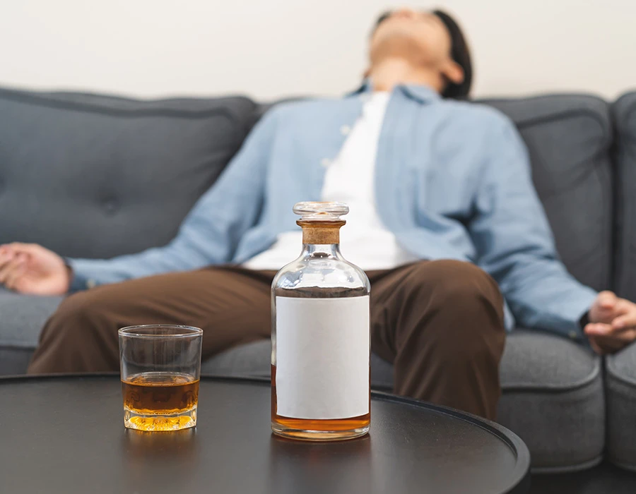 Persoon zit uitgeput op de bank met alcohol op tafel.
