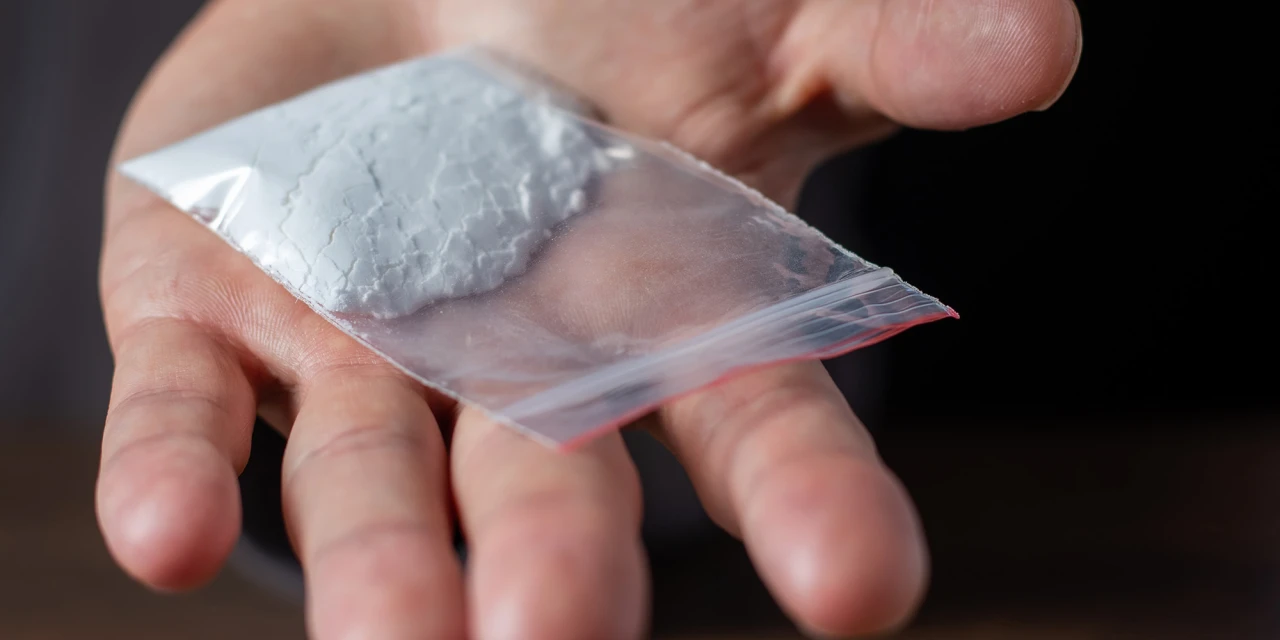Hand met zakje wit poeder laat verschil tussen harddrugs en softdrugs zien.