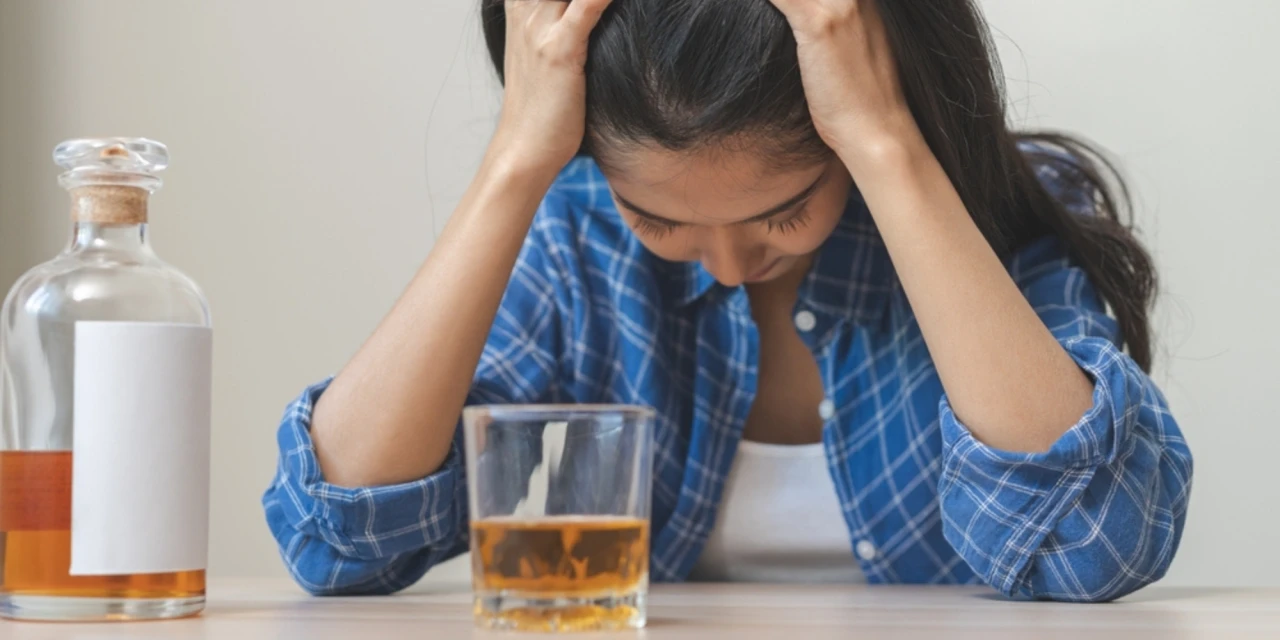 Hulp bij alcoholverslaving voor een vrouw die radeloos naast haar glas alcohol zit.