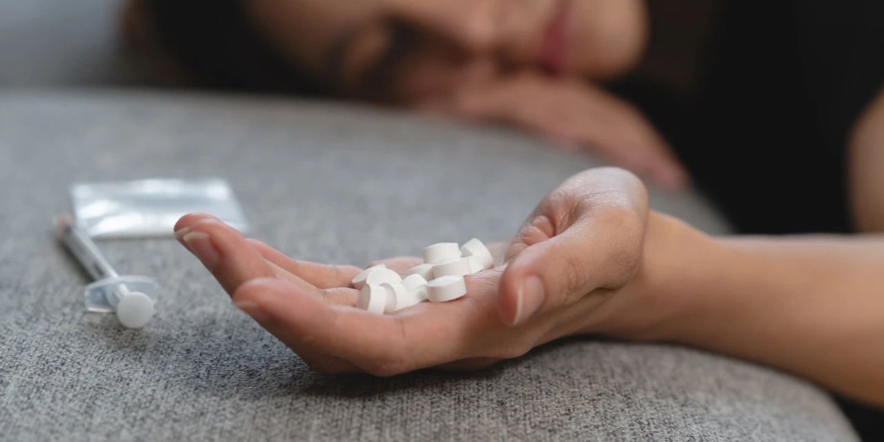 Hand met pillen op bank verwijst naar opioïdenverslaving.
