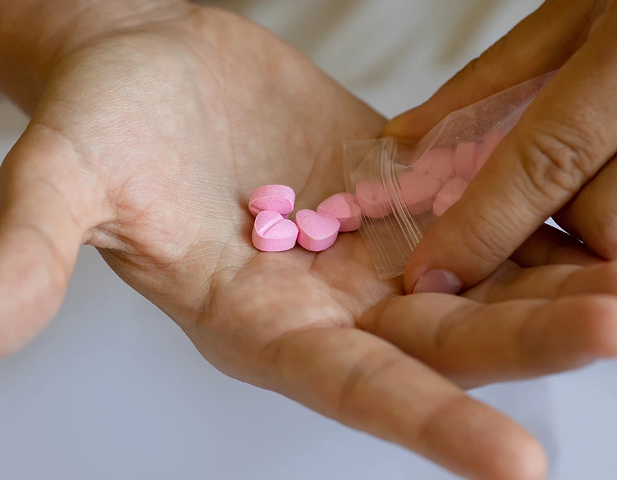 Hand giet roze pillen uit zakje in hand als symbool voor MDMA-verslaving.