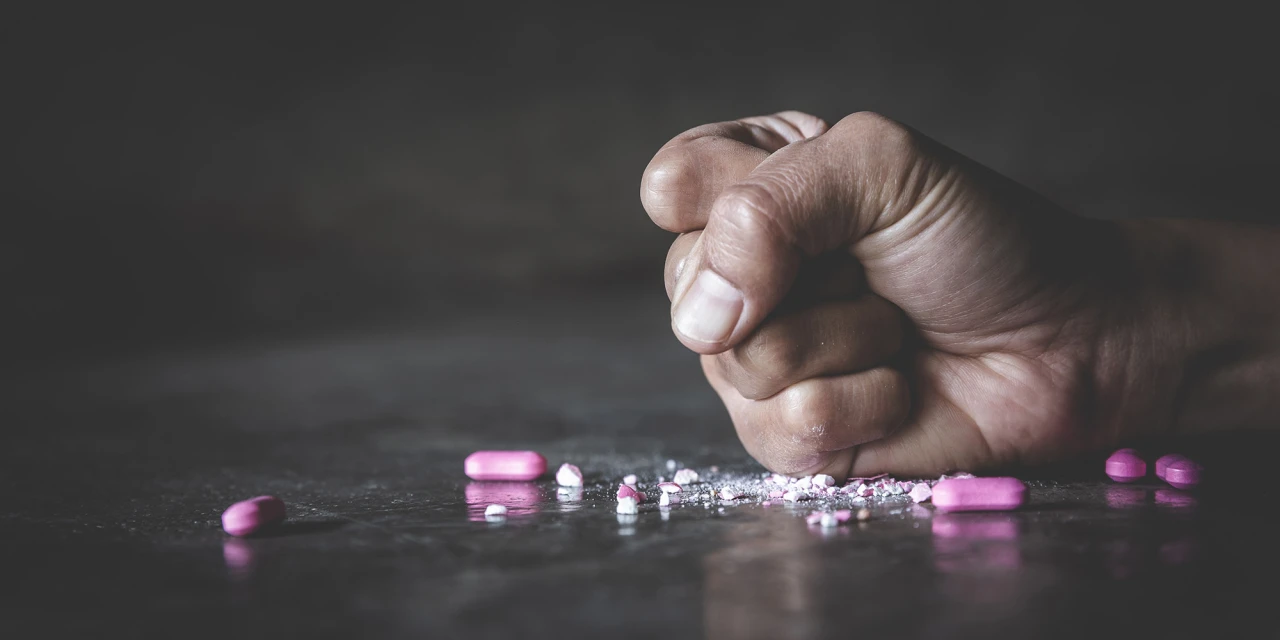 Hand die op tafel slaat met tusi of roze cocaïne en gebroken roze pillen eromheen.