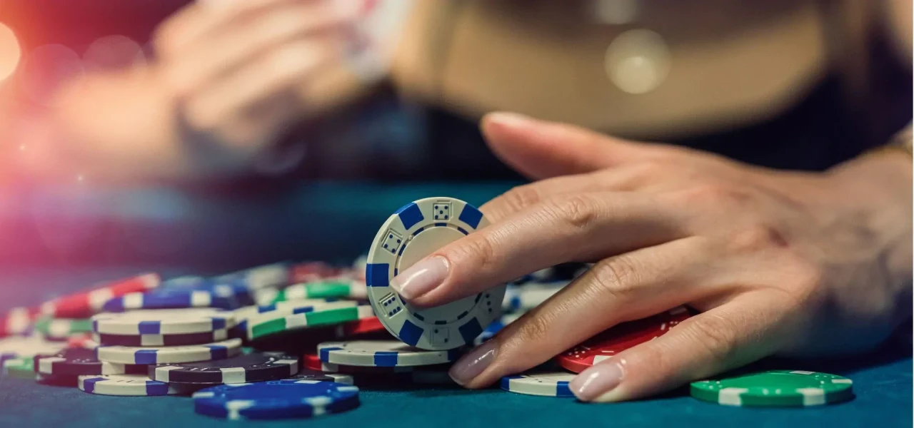 gokfiches-in-vrouwenhand Tafel vol met gokfiches en een vrouwenhand die een van de fiches vast heeft.