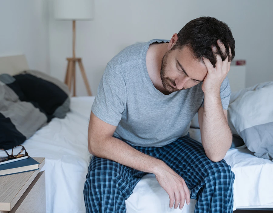 Man zit op bed met hand in haar, oogt uitgeput, beeld van PTSS-klachten.