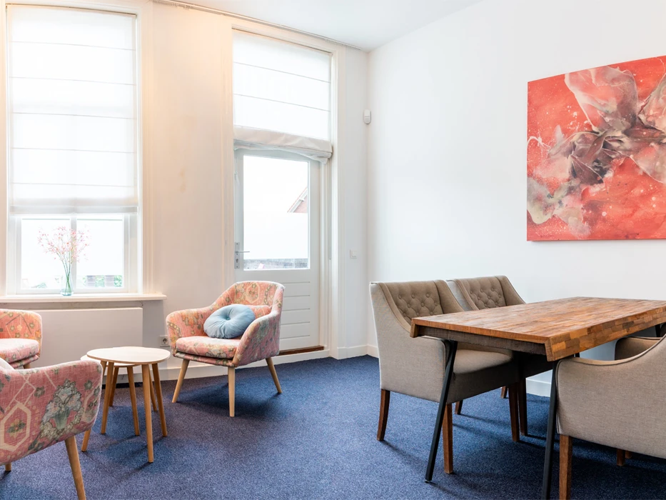 afkickkliniek-fazantlaan-leefruimte Lichte kamer van polikinische verslavingszorg Eindhoven, met diverse zitplekken en een schilderij.