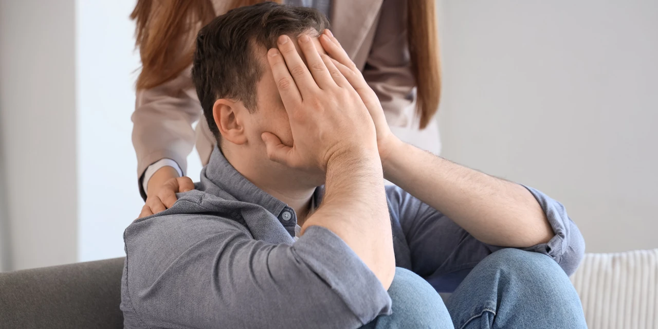 Man met handen voor gezicht krijgt steun van partner tijdens alcoholverslaving.