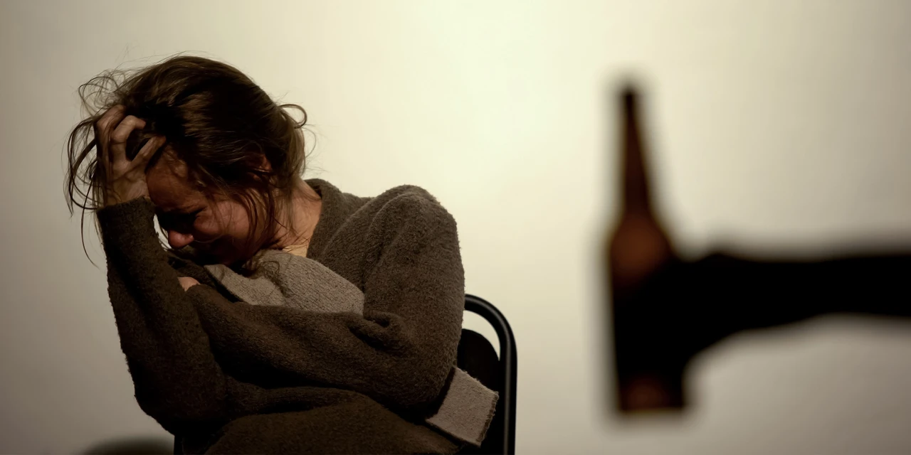 Vrouw met hoofd in handen tijdens afkickverschijnselen alcohol, met lege fles op achtergrond.