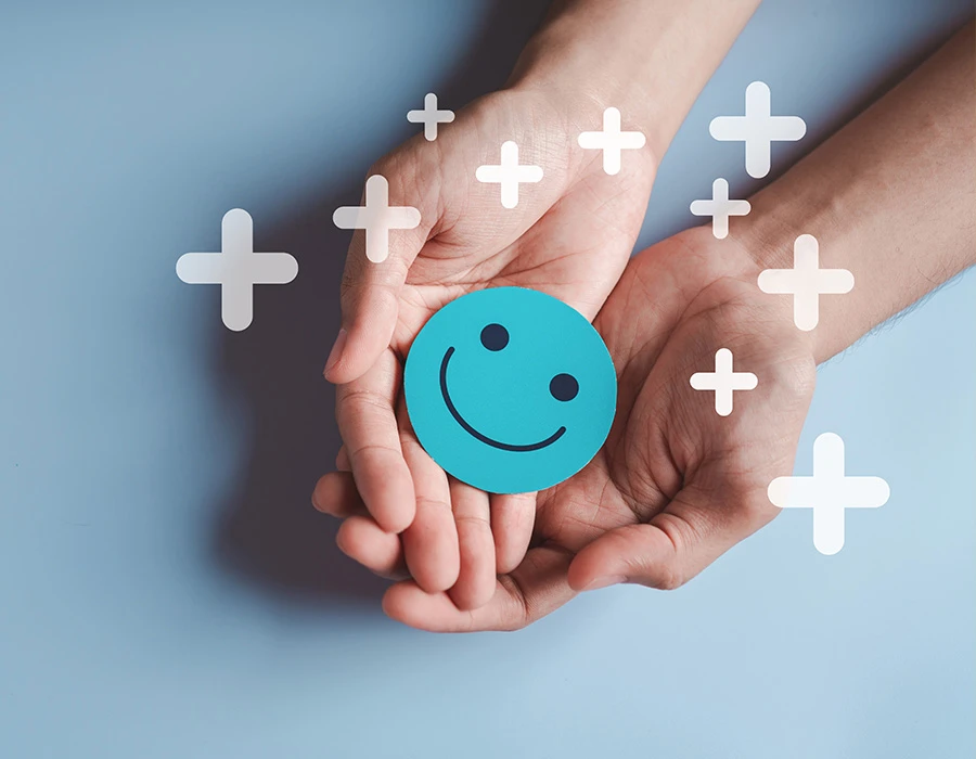 Twee handen houden een blauwe smiley vast tussen witte plustekens, ter illustratie van dopamine.
