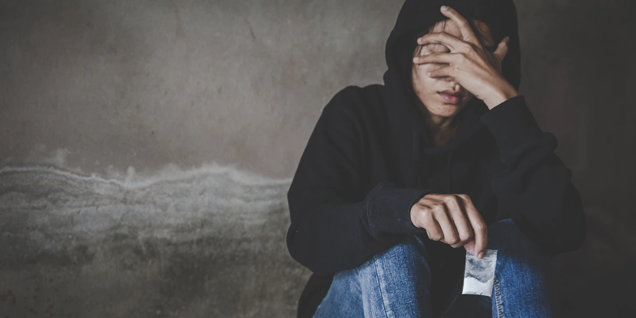 Persoon zit verdrietig tegen muur met zakje drugs en denkt aan stoppen met coke.