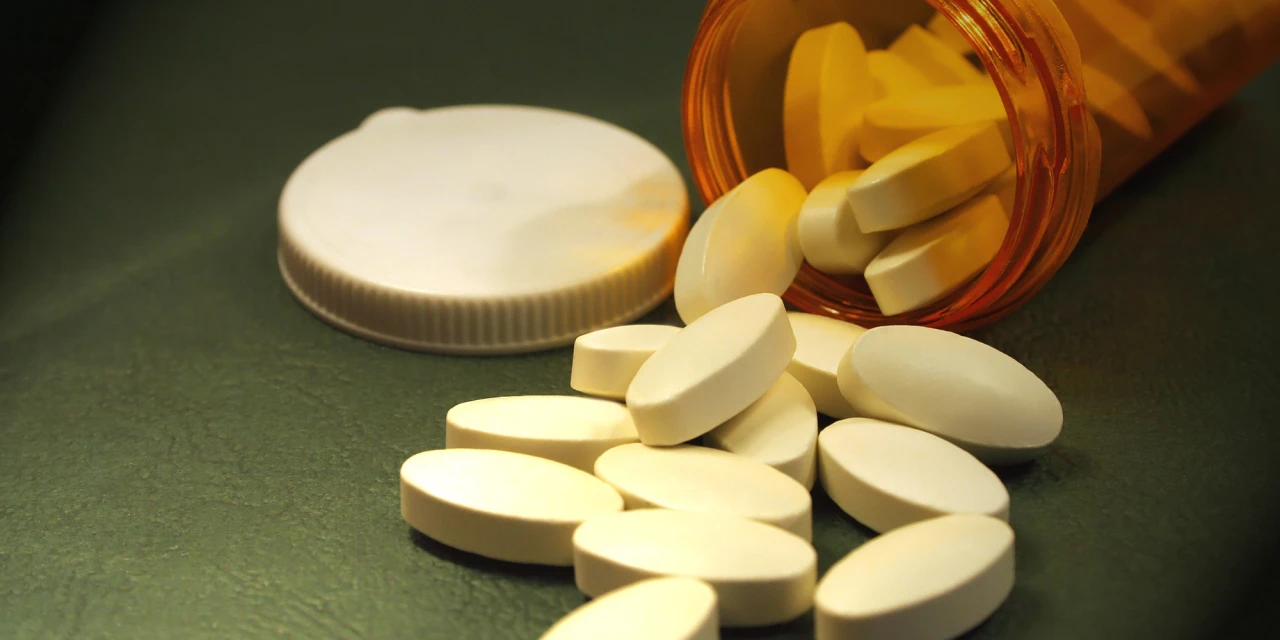 Open potje met oxycodon waar witte tabletten uit liggen op een tafel.