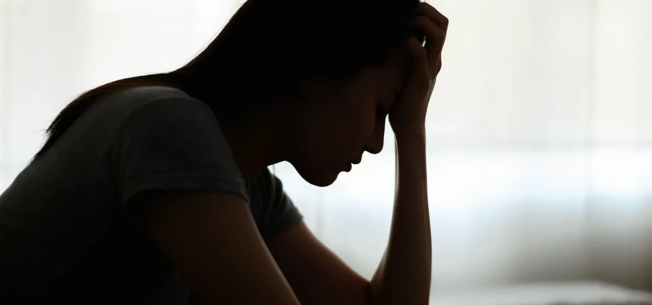 depressieve-persoon-met-hoofd-in-hand Silhouette van een depressieve vrouw met het hoofd in haar hand tegen een lichte achtergrond.