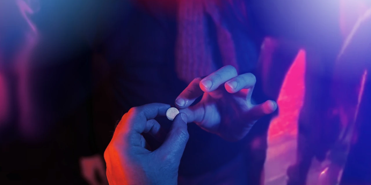 Hand geeft pil door in clublicht als beeld van MDMA-verslaving.