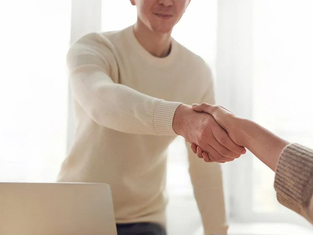 handen-schudden Twee personen schudden de handen voor een met licht overgoten raam.