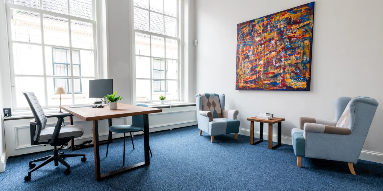 Gesprekskamer met bureau en stoelen in lichte ruimte.