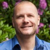 Bastiaan Meyers, medisch directeur bij Connection SGGZ, staat buiten voor een struik met roze bloemen en glimlacht.