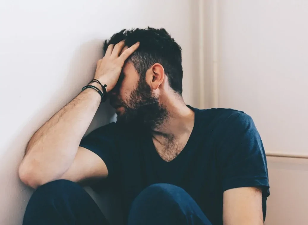 depressieve-man-tegen-muur Depressieve man zittend tegen de muur met zijn hoofd in de hand.