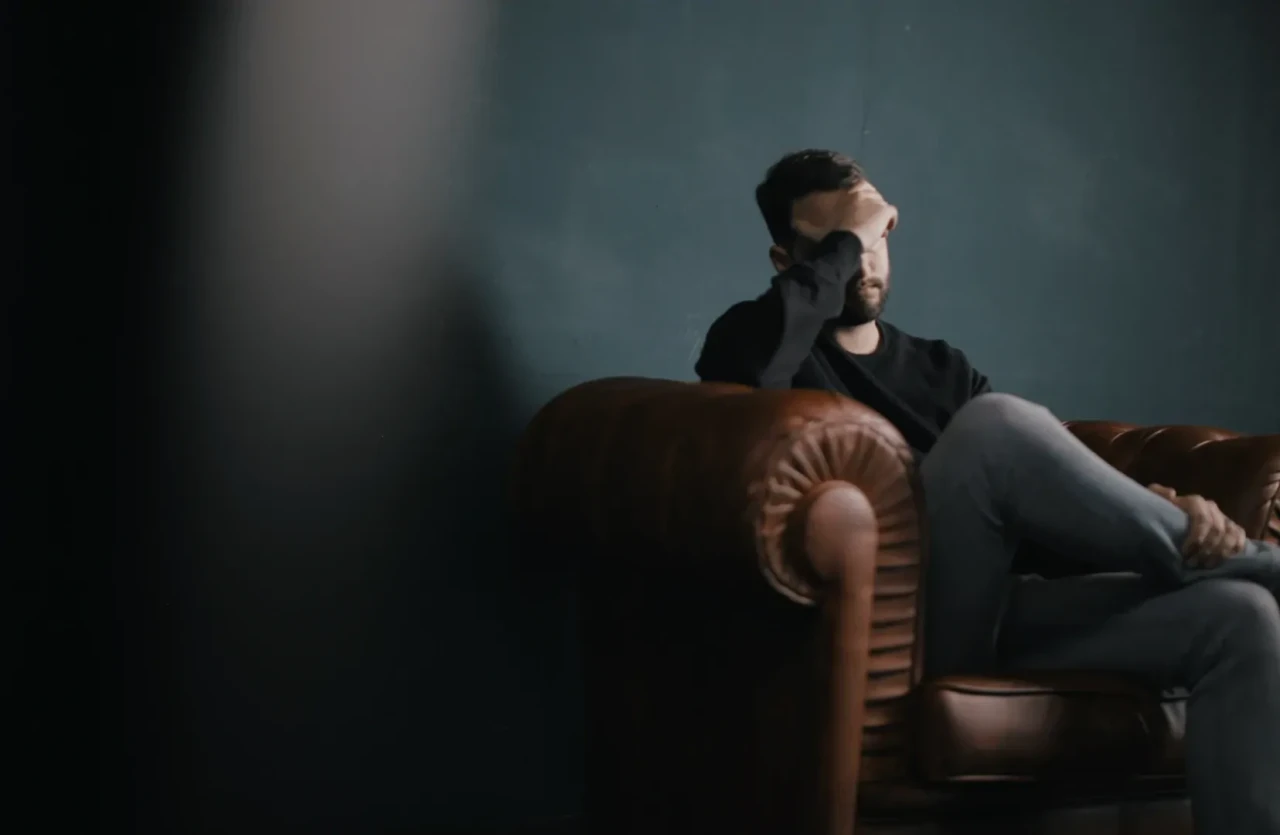 depressieve-man-op-bank Donkere foto van een depressieve man op bruine bank met het hoofd in de hand.