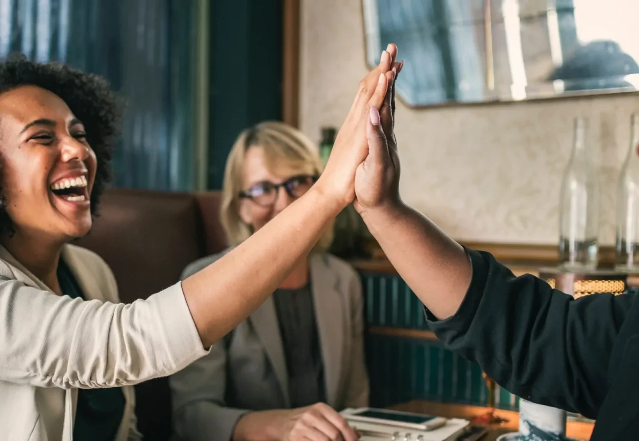 high-five-lachende-vrouw Twee blije mensen geven elkaar een high five, op de achtergrond lacht een vrouw.