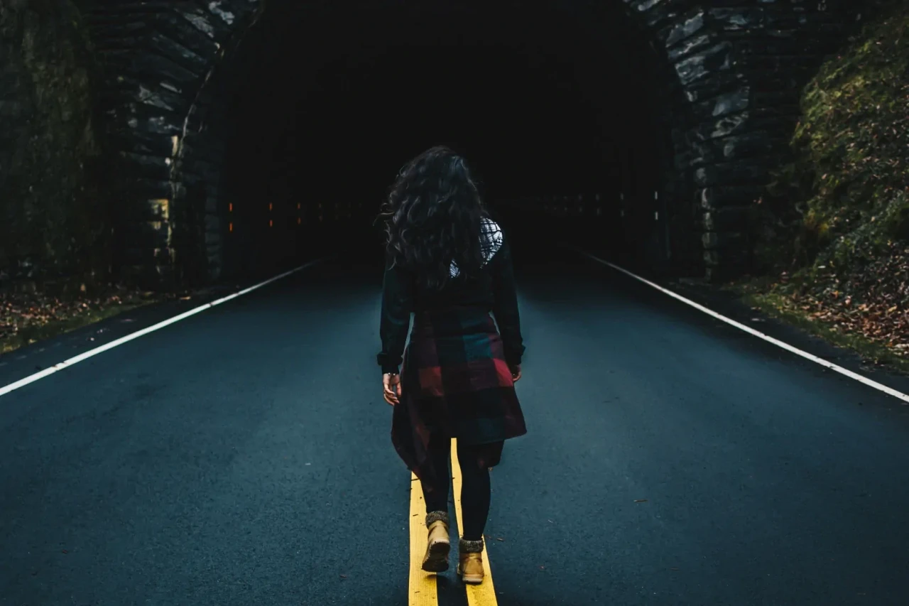 wandelende-vrouw-tunnel Wandelende vrouw met donker haar die richting een tunnel in de bergen loopt, over een gele streep.