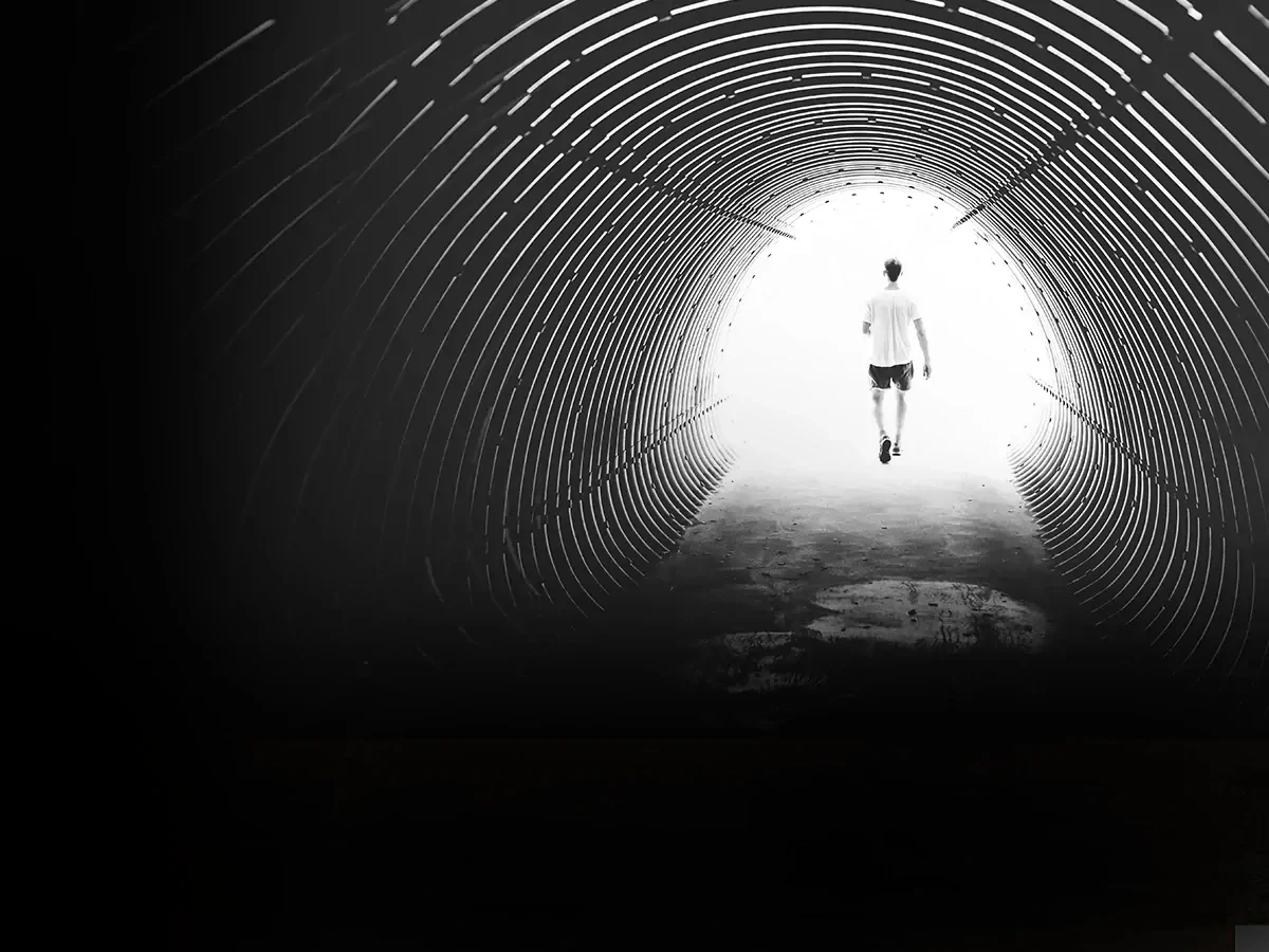 man-lopend-door-tunnel Zwart-wit foto van een man in korte broek en wit t-shirt lopend door een tunnel.